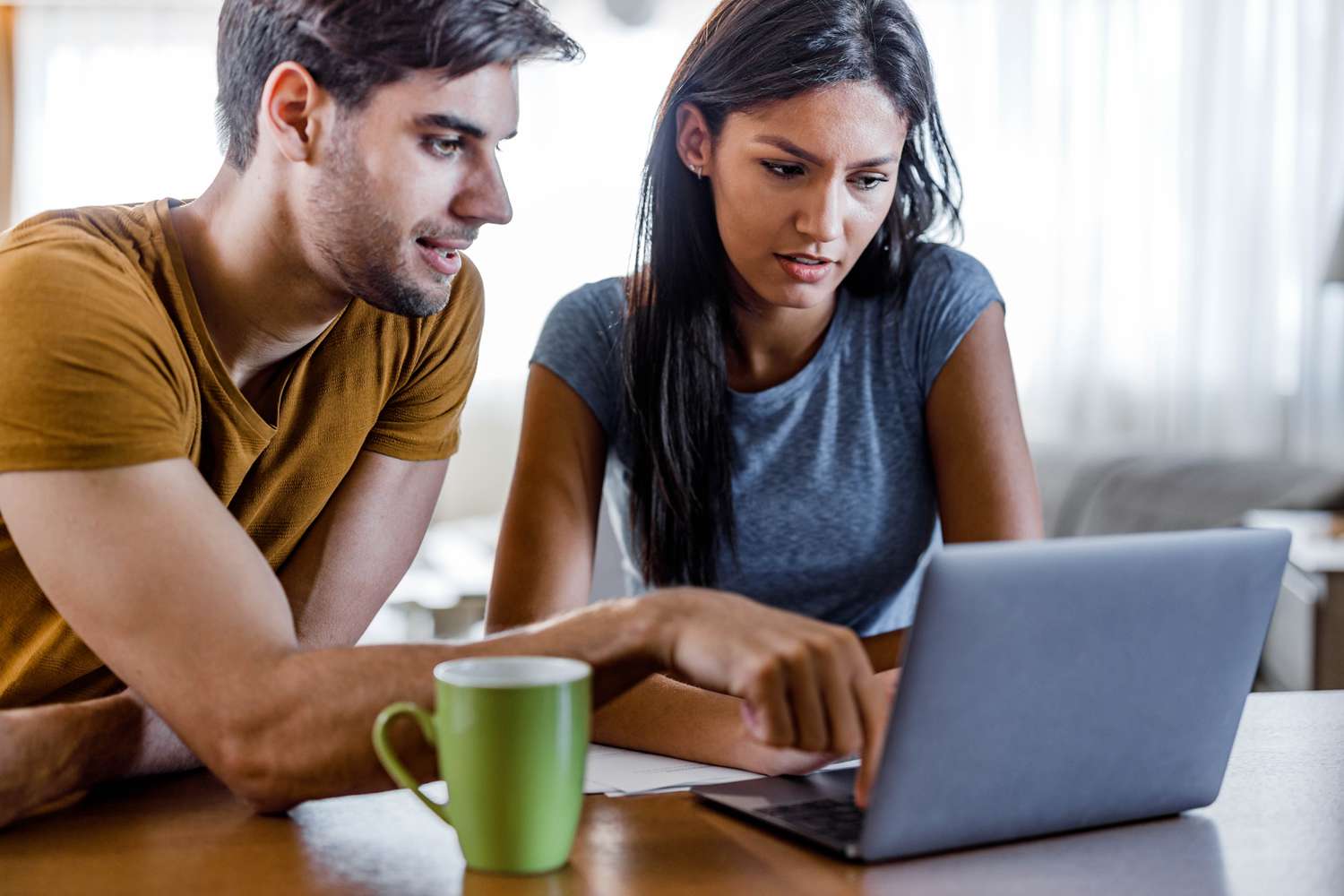 A man and a woman sit at a desk looking at a laptop