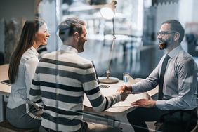 Happy Couple Shaking Hands With Real Estate Agent in the Office