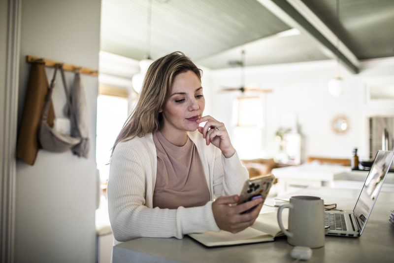 A woman sits at a kitchen counter looking at a smartphone