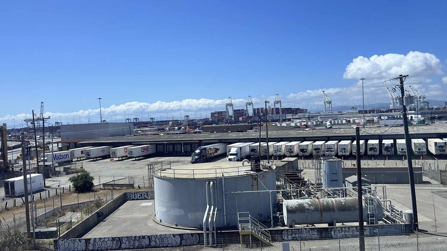 Shipping containers, trucking operations, and industrial storage tanks at the Port of Oakland on a clear day, West Oakland, California, May 2025