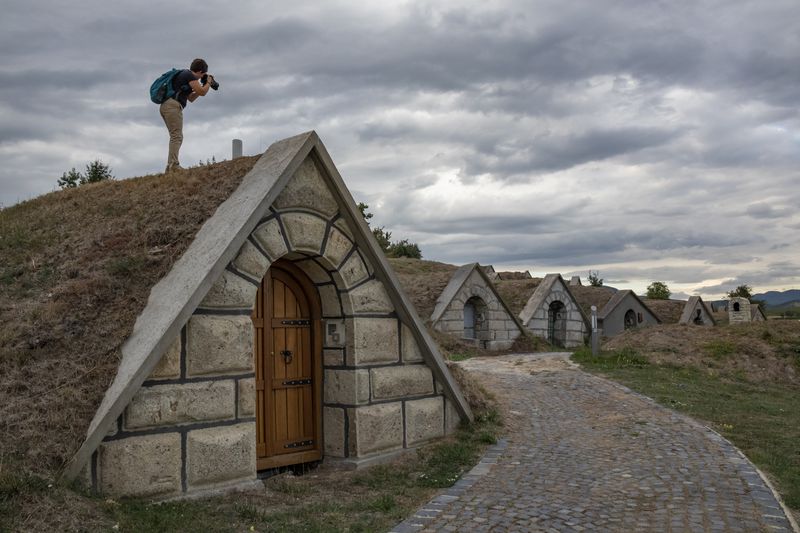 Person photographing small, triangular-roofed buildings extending along a cobblestone pathway