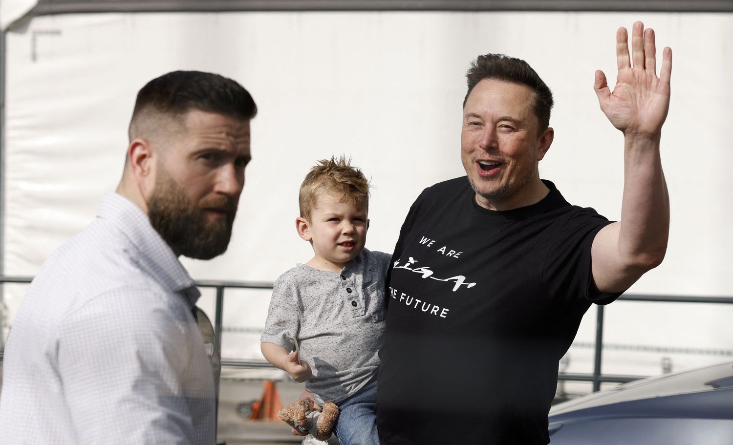 Elon Musk waving to fans while carrying his son.