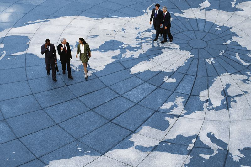 Groups of professionally dressed business people talk as they walk across an open plaza that is decorated to look like a globe.