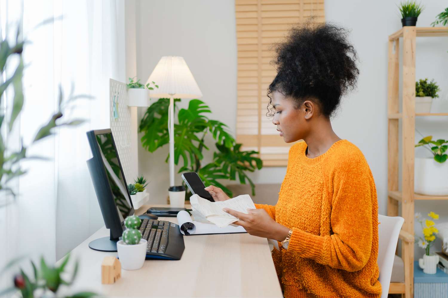 Woman sitting at desk with receipts in one hand and phone in the other.