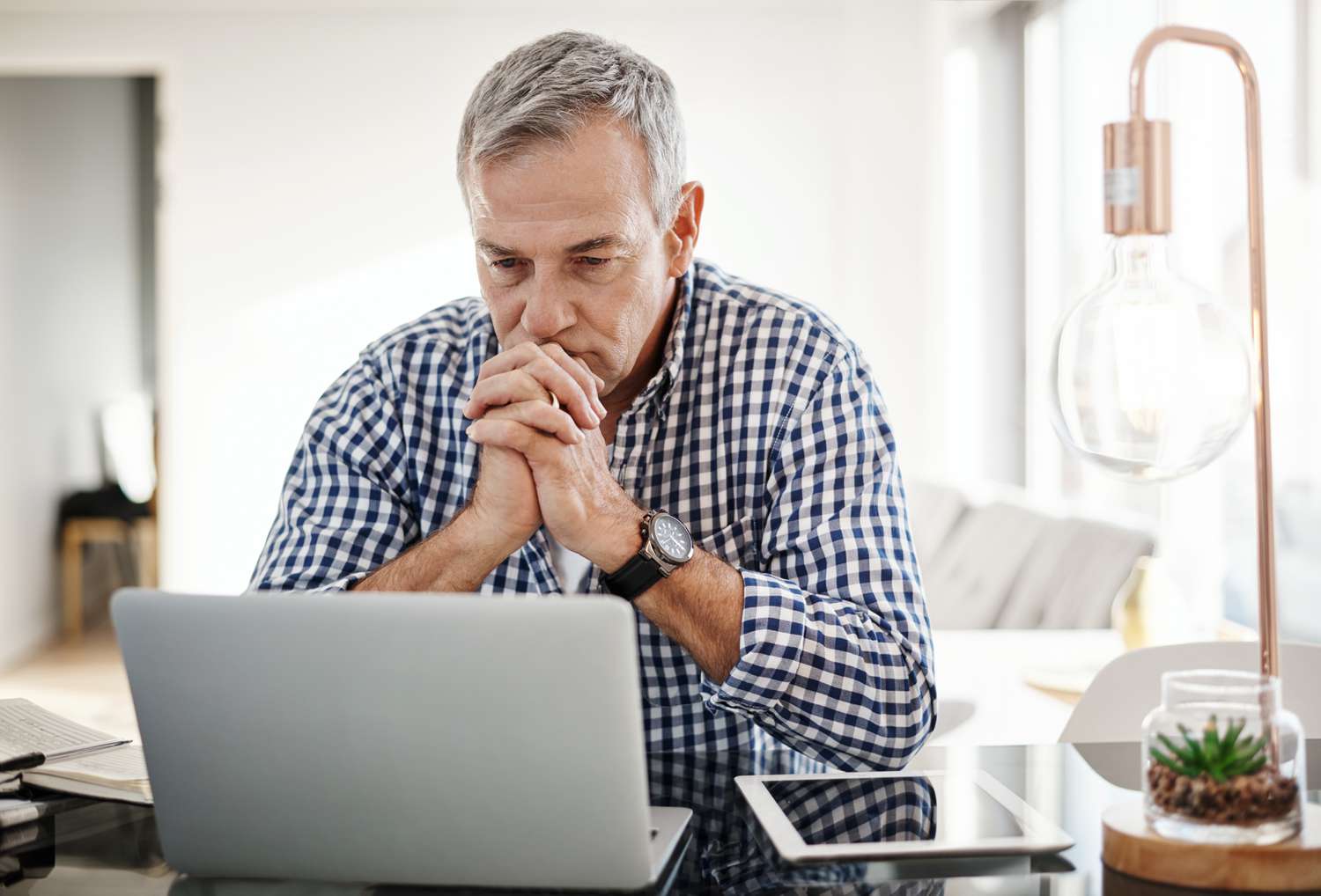 Older ma sitting at home and looking intently at something on his laptop