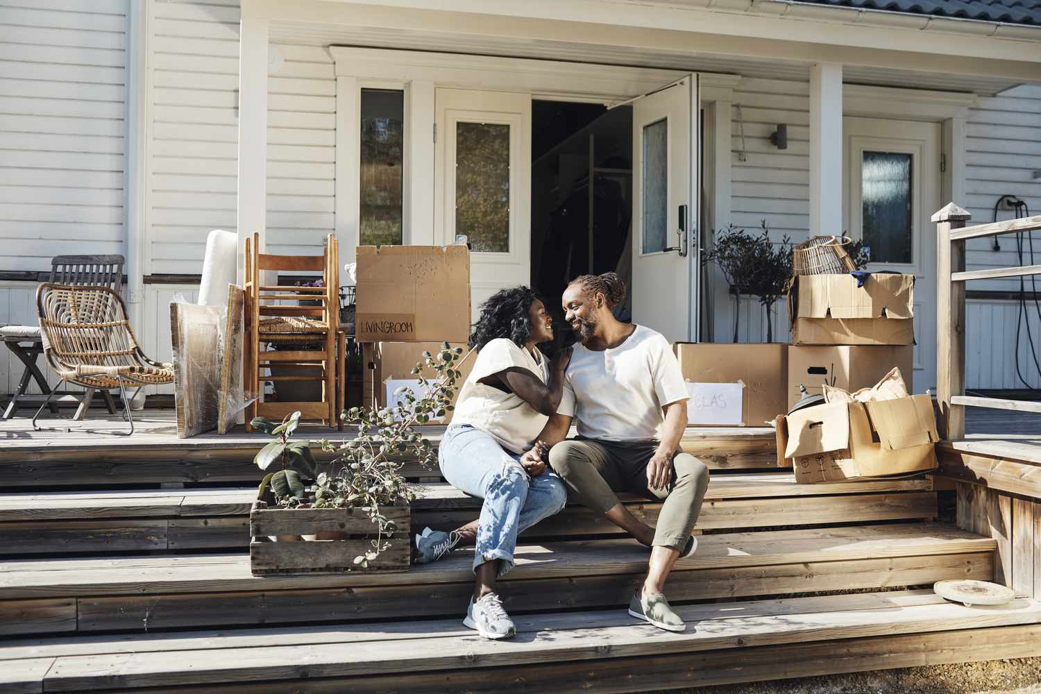 A man and a woman sit on the front porch of a house with moving boxes around them