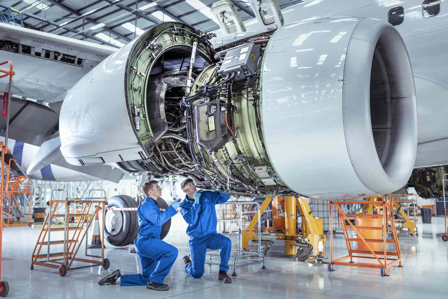  Aircraft maintenance engineers work underneath large jet engine.