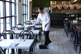 A woman sweeping the floor of an empty restaurant