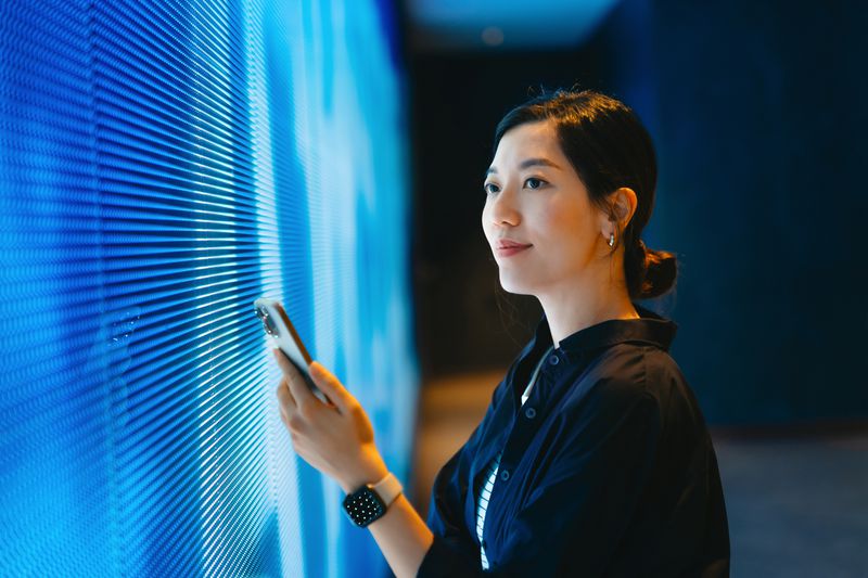 A person standing in front of a large digital screen and holding a cell phone