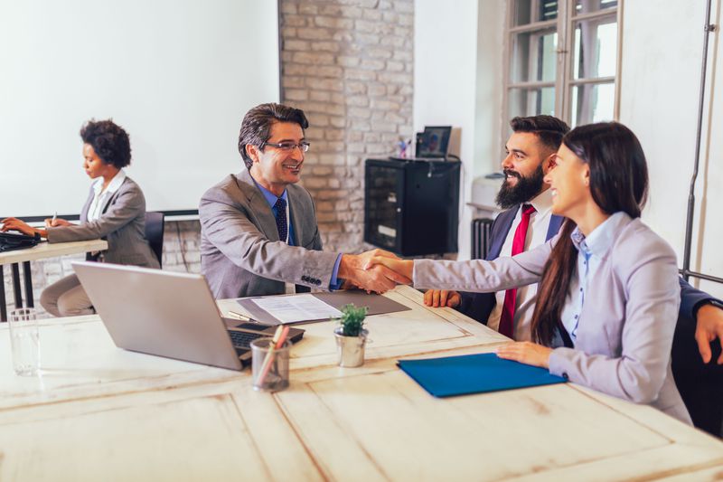 Two people shaking hands in an office meeting with a third person looking on