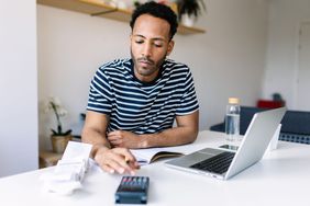 Man doing paperwork with a calculator and laptop