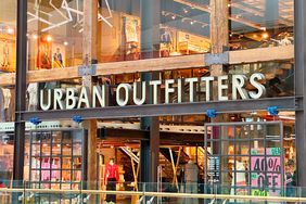 An Urban Outfitters sign is seen above the entrance to a brightly lit store with clothes inside.