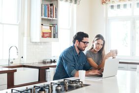 A man and a woman sit at a kitchen island with a laptop