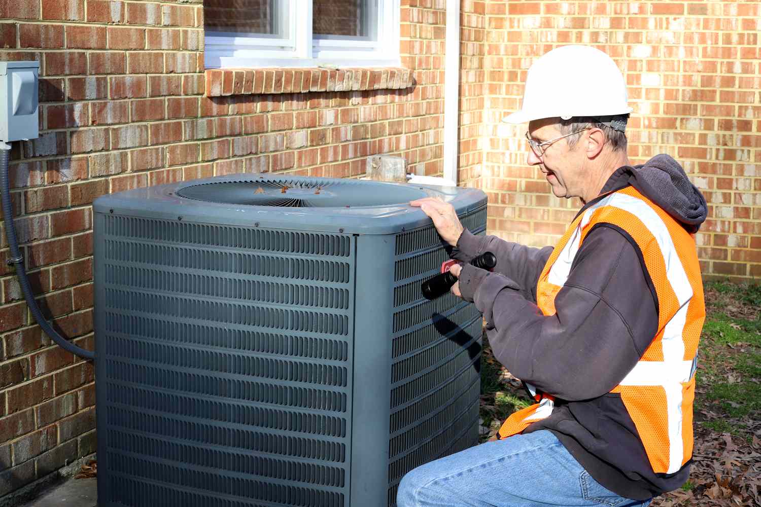 Maintenance worker looking at air conditioner unit outside home