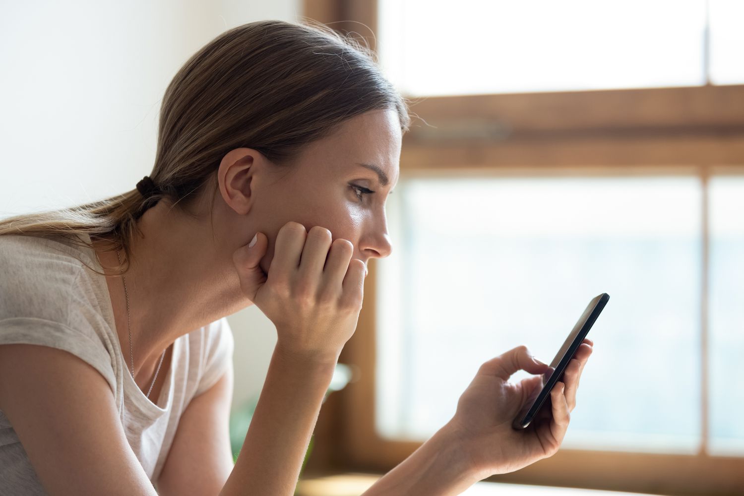 Young woman at home looking seriously at something on her smartphone