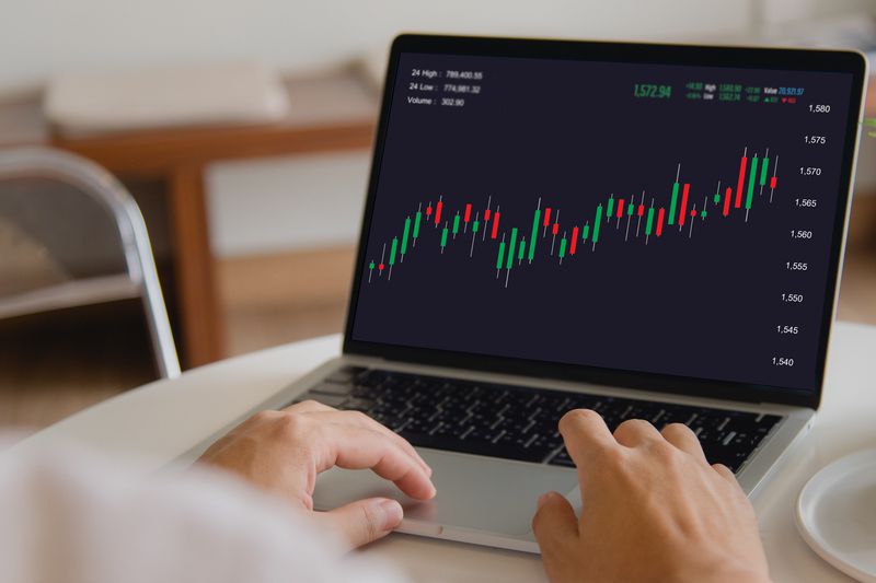 A trader uses a laptop to examine technical trading patterns shown on a candlestick chart. 