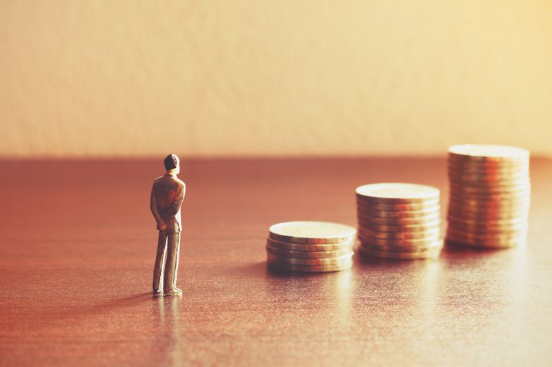 A miniature person looking at three large stacks of coins