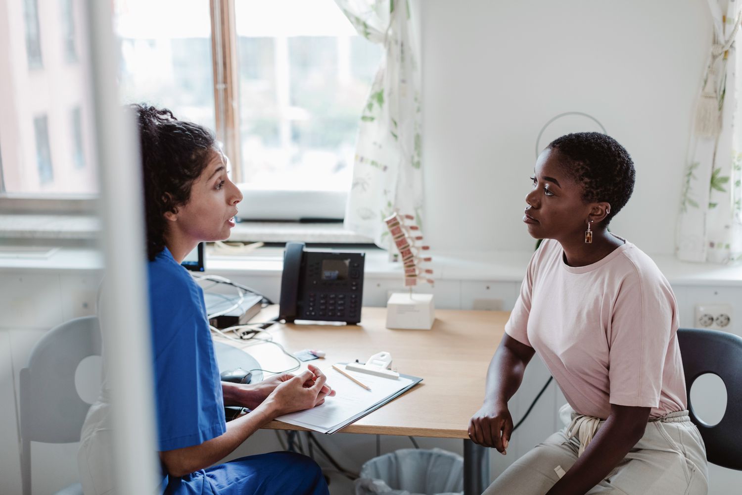 A woman medical provider speaks with a female patient in an office