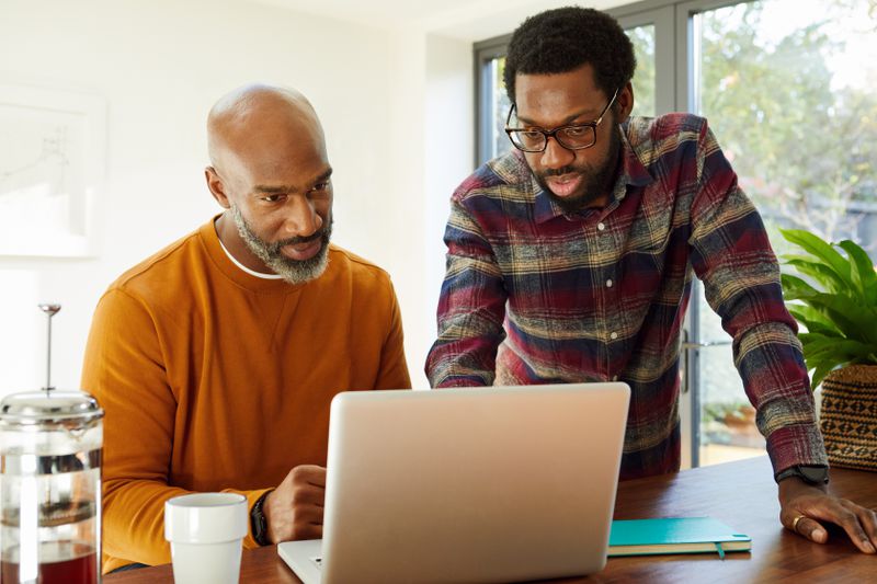 Young man and older man using laptop in kitchen