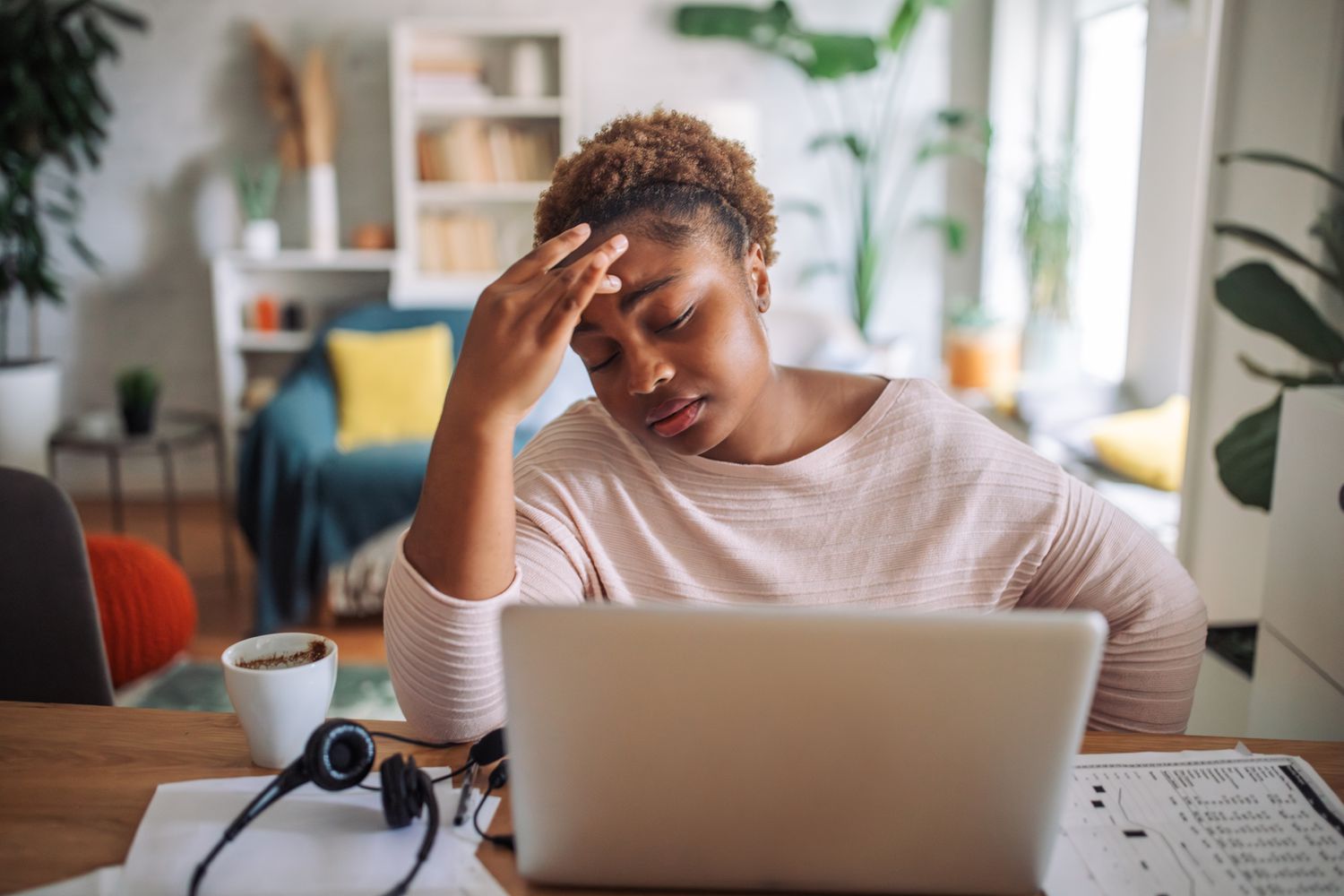 A woman at a desk clutches her forehead.
