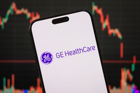 The GE HealthCare logo is seen on a phone screen with a stock chart in the background.