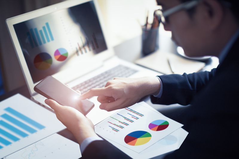 A businessman hand working on smartphone and laptop computer with financial business graph information diagram.