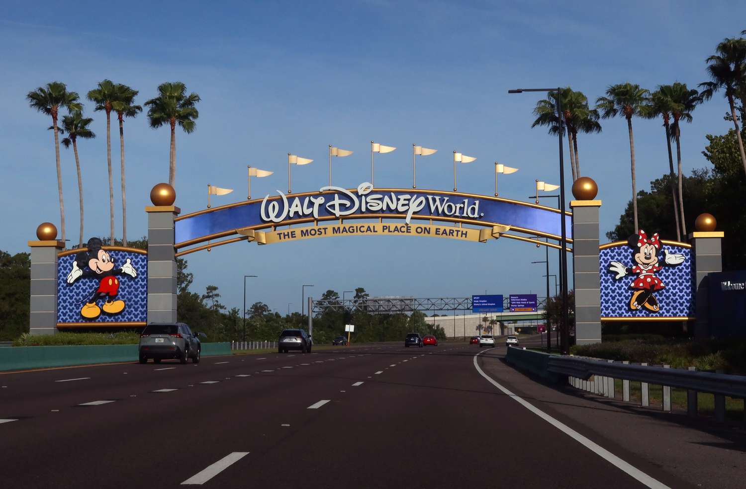 Cars drive toward the entrance of Walt Disney World in Florida, through an arch with Mickey and Minnie Mouse on each side.