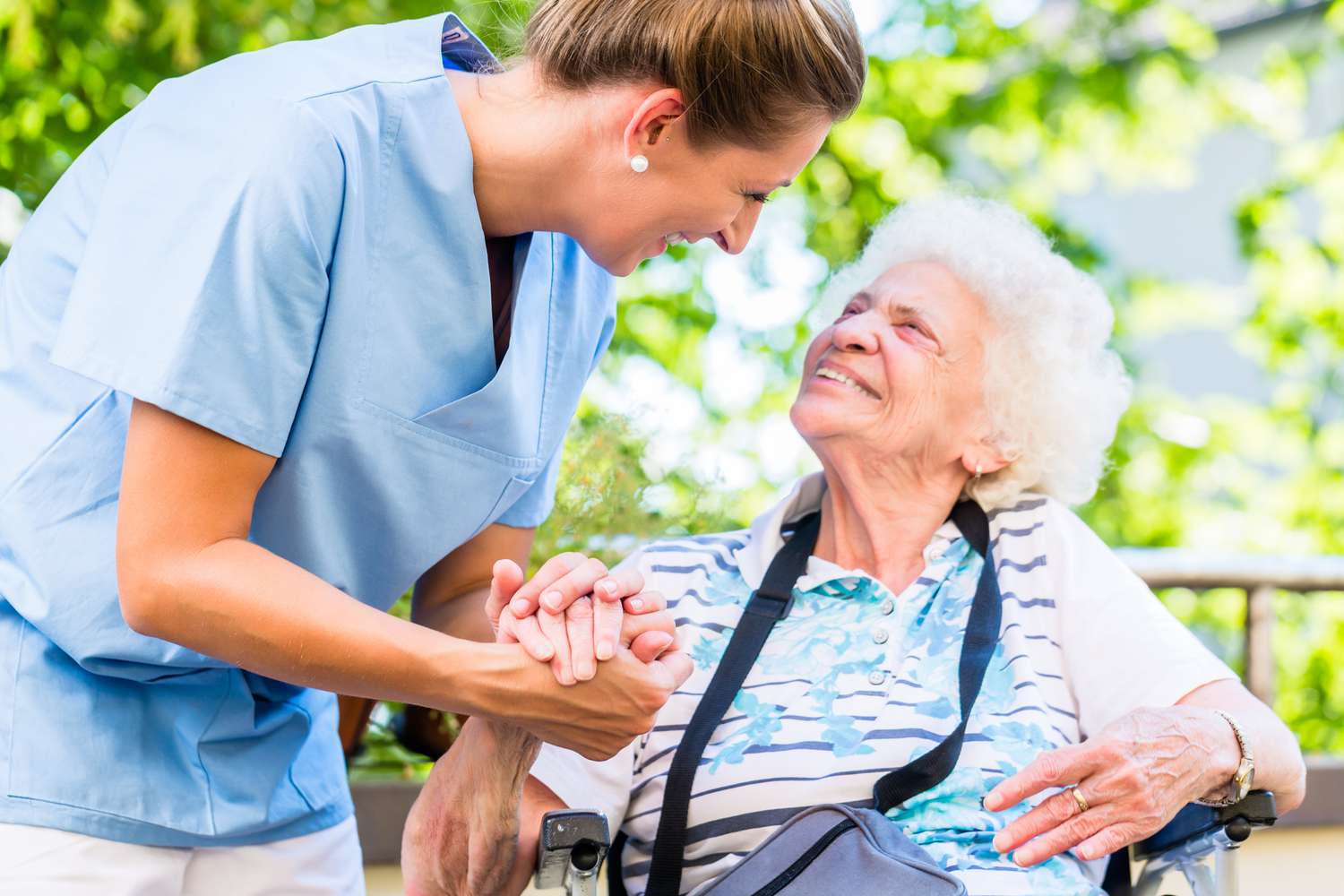 A nurse holds the hand of an older woman in a nursing home.