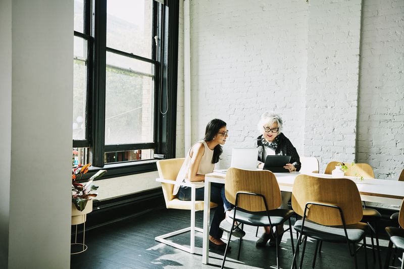 Two women talking at a table, looking at a tablet or notepad