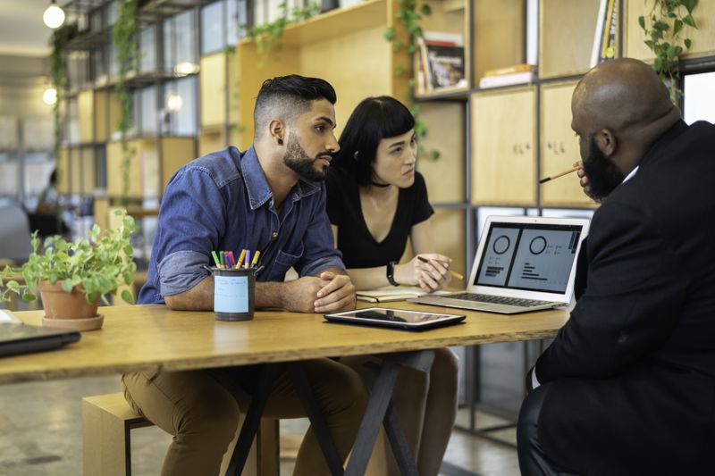 Couple talking with someone displaying a laptop screen in an office