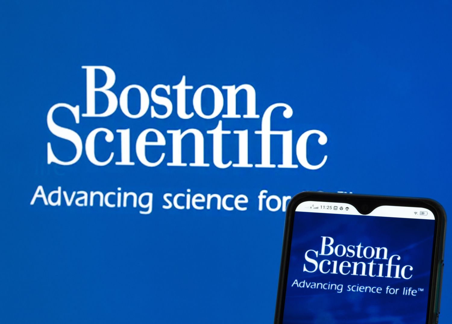 A Boston Scientific Corporation logo seen displayed on a smartphone and pc screen in the background