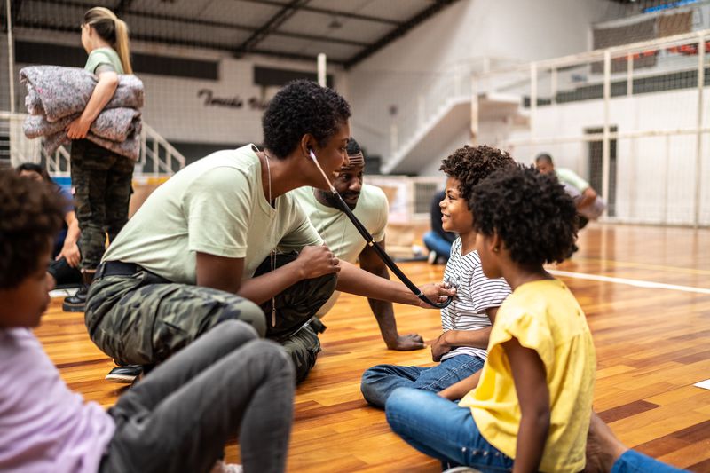 Army doctor leaning down in gymnasium to help children