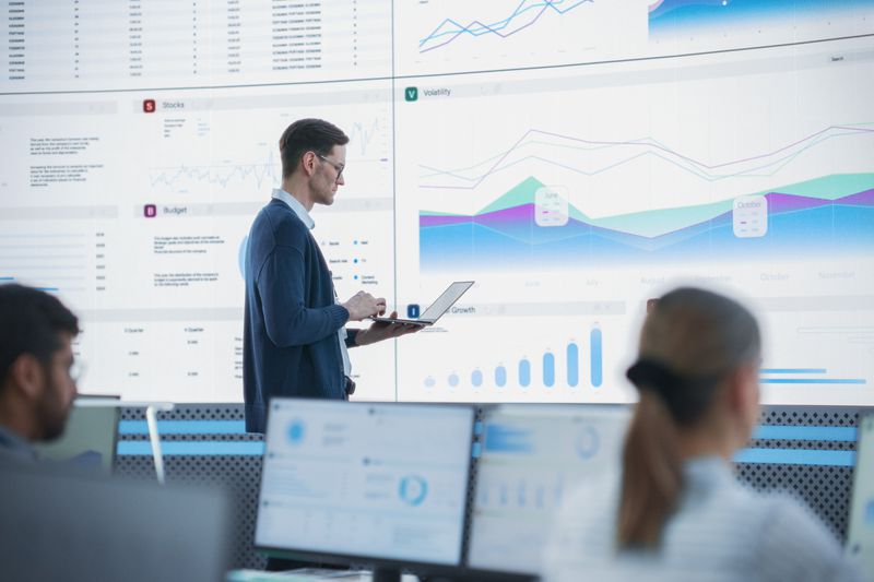 A senior financial analyst reviewing information and reports on big digital screen in modern monitoring office.
