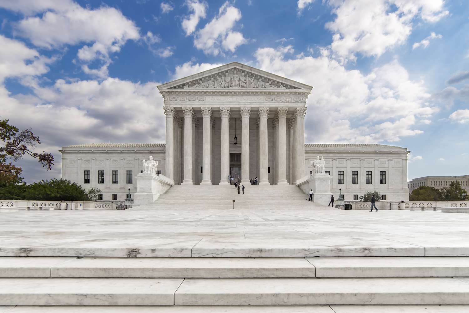 The Supreme Court building, centered under a blue sky with some scattered clouds.