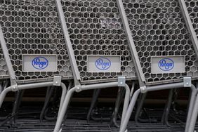 The blue Kroger logo is seen on 3 gray shopping carts that are stacked together left-to-right.