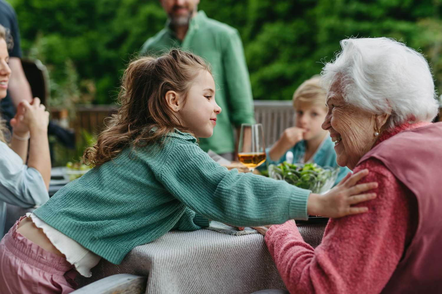 Small child talking to older family member in an outdoor setting at a table.