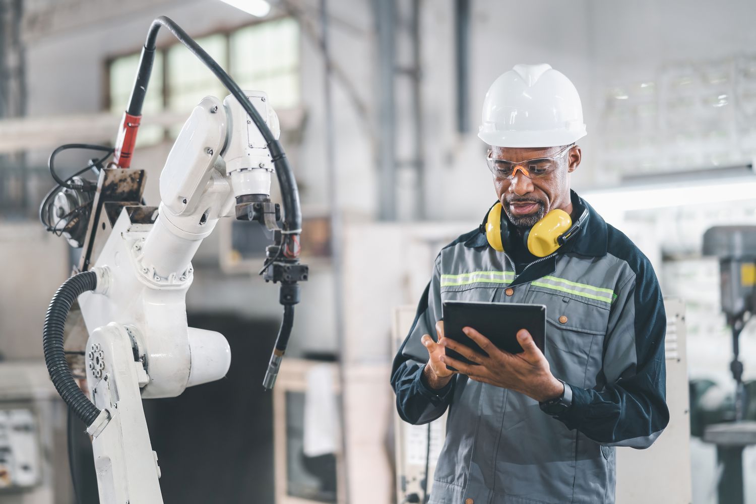 worker on tablet controlling robot arm