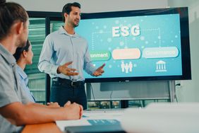 Team gather around a conference room with a flat screen depicting the three parts of ESG.