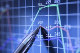 A financial analyst pointing with a pen on a monitor showing charts.