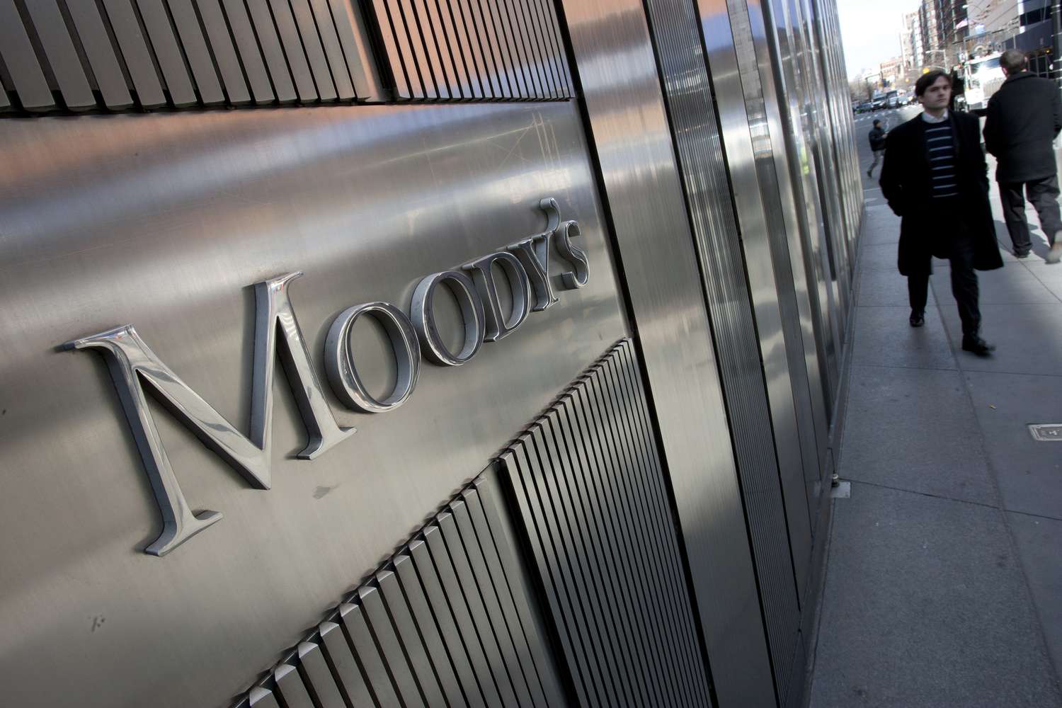 The Moody's logo on a building, pedestrians walking on the sidewalk