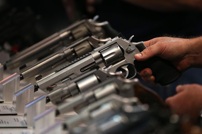 A hand holding a display pistol at an NRA exhibition symbolizes the high rate of gun ownership in the United States, which far outpaces other nations.