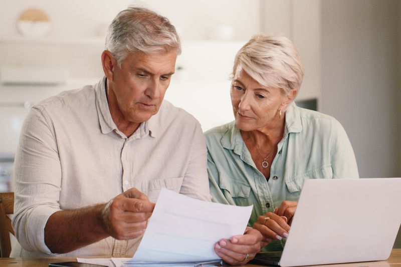 Older couple sitting at home and looking together at mortgage documents and a laptop