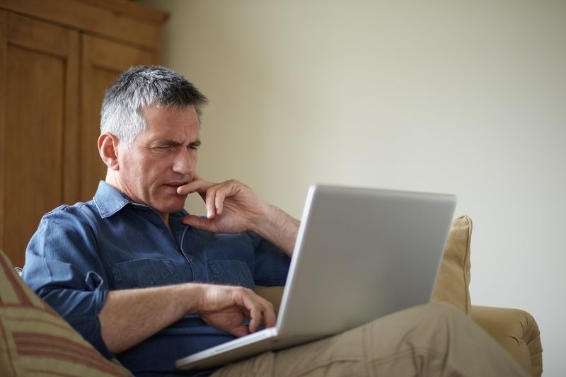Man in his 50s sitting at home and looking very seriously at bank rates on his laptop