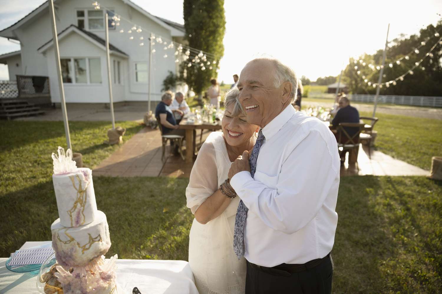 Affectionate, happy senior bride and groom hugging at wedding cake in sunny rural garden