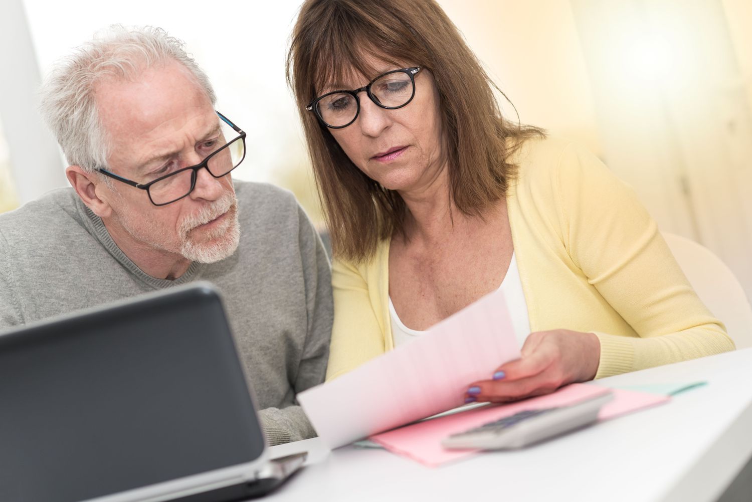 Couple in their 50s or 60s sitting at home and looking at mortgage documents and a laptop