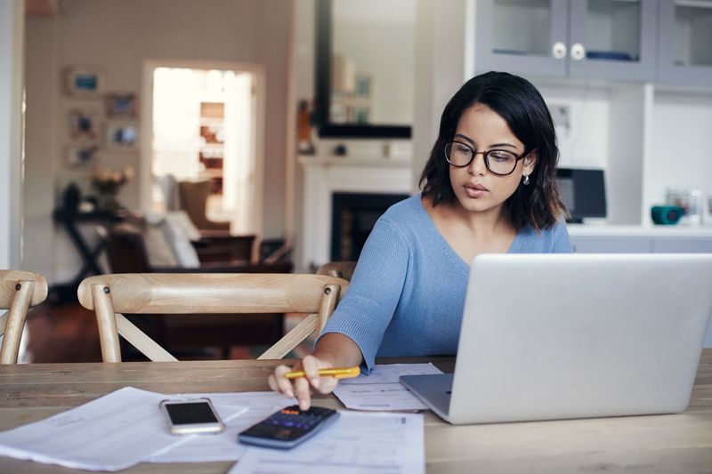 An investor reviews calculations using laptop and calculator