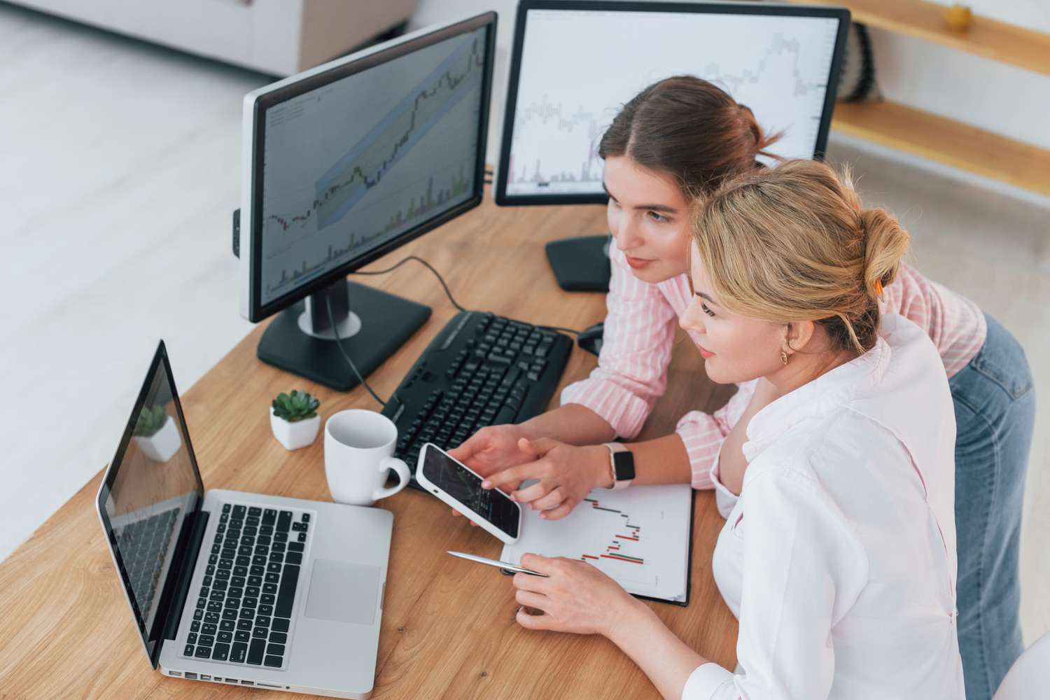 Two traders work together at an office desk looking at various computer screen and discuss a speculative trade.