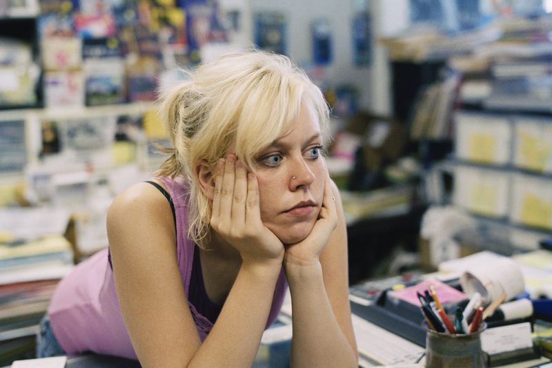 A small business owner leans on the service counter in their store while they wait for business to pick up.