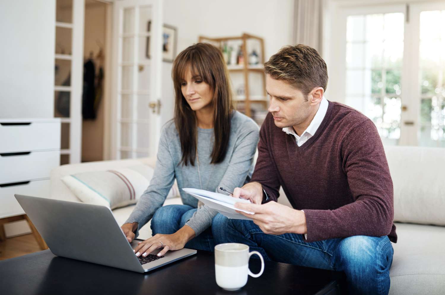 Couple in their 30s sitting in their living room and looking at a laptop together