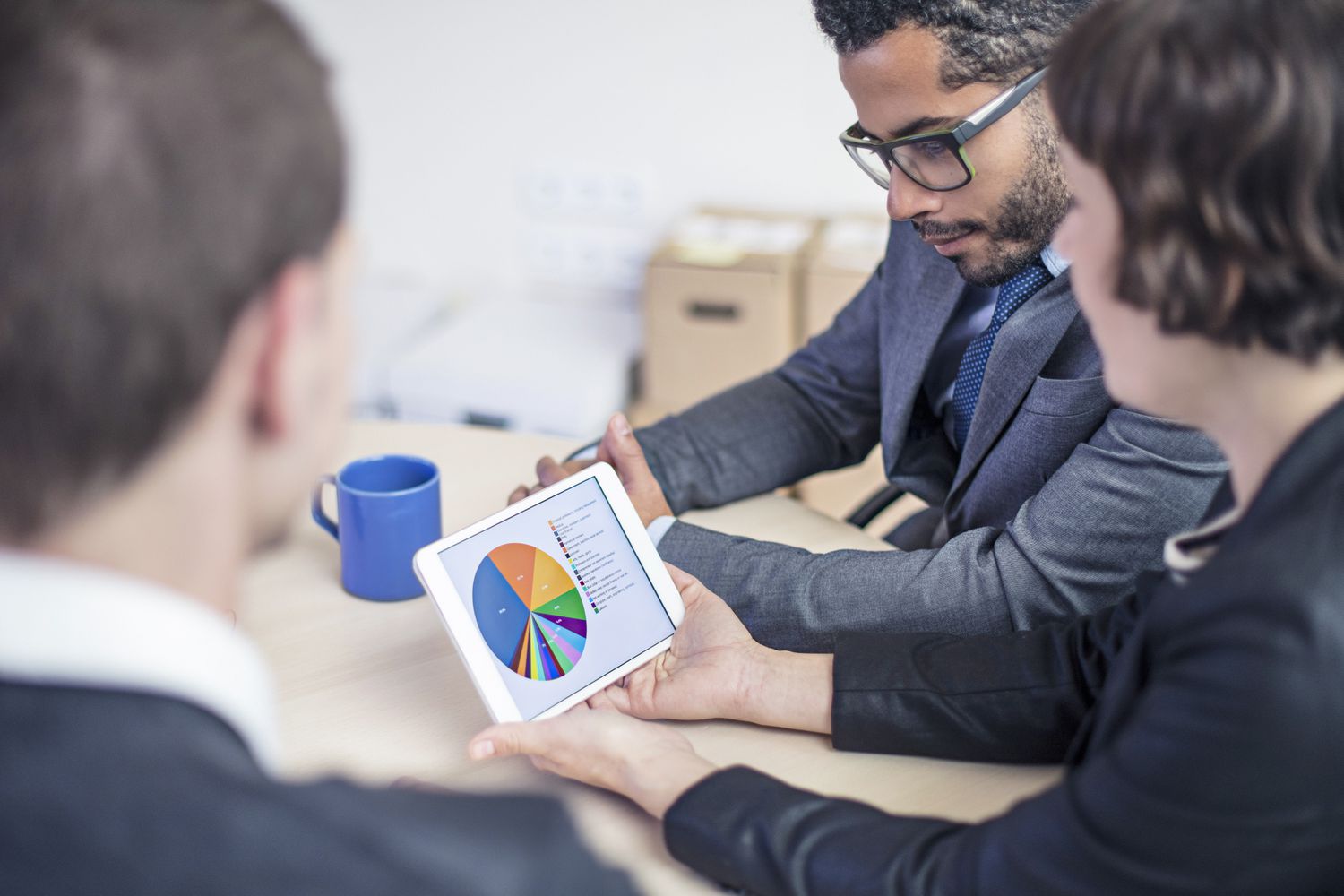 A financial advisor uses a pad computer displaying a pie chart to explain current portfolio allotment to two clients.